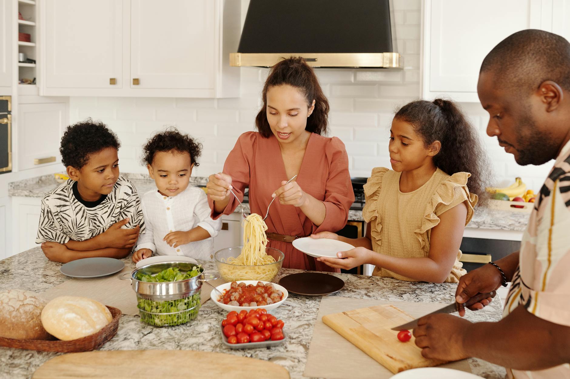 Family cooking together in a modern kitchen, preparing pasta and fresh vegetables.