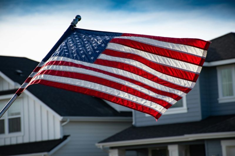 American flag waving in front of a suburban house, representing patriotism and homeownership.