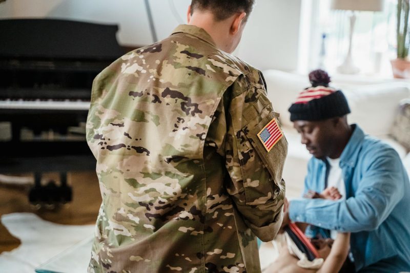 A soldier in camouflage uniform hugs family members in a cozy home setting, conveying warmth and connection.