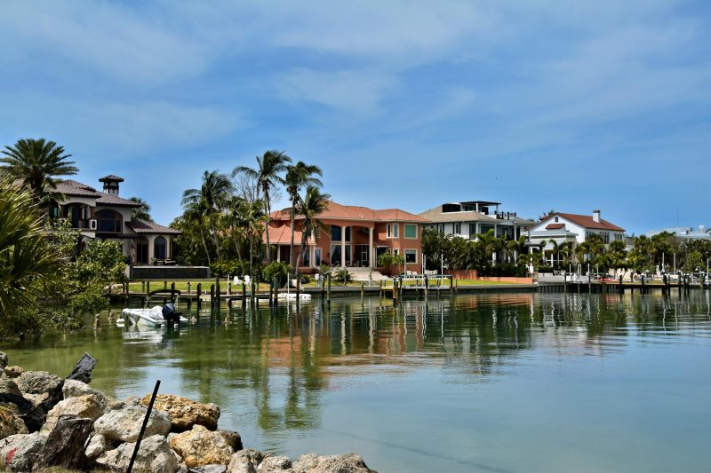 Luxury homes along a waterfront, framed by palm trees and calm waters in a tropical setting.