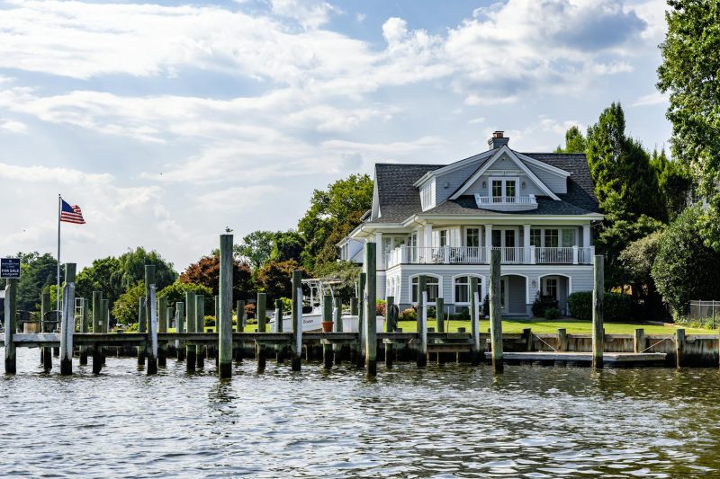 Waterfront home with dock and American flag under a clear blue sky on a sunny day.