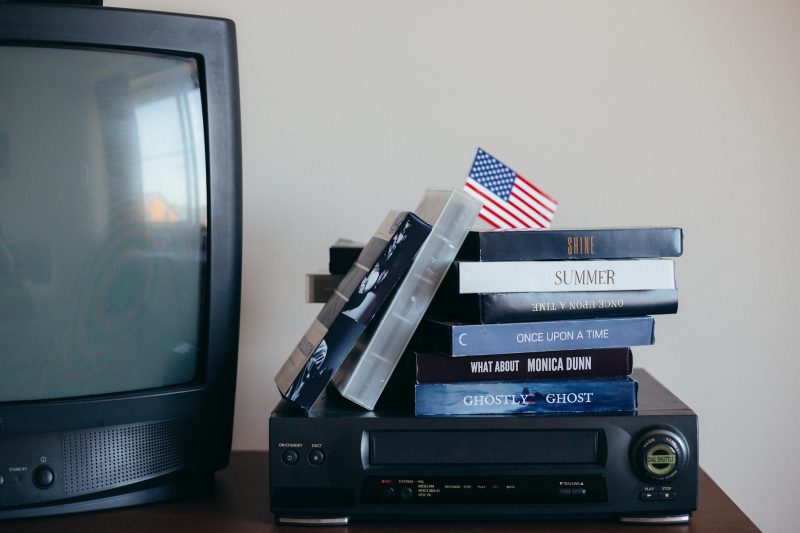VHS tapes, a vintage TV, and a small American flag on a table create a nostalgic scene.