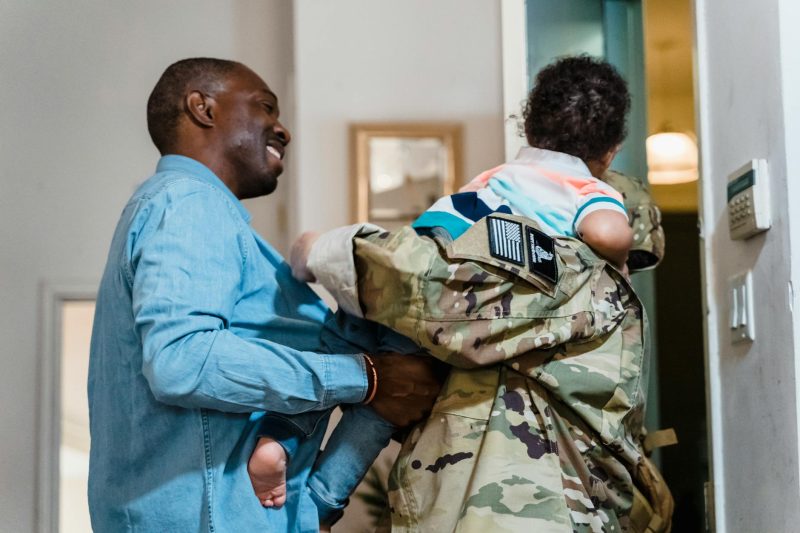 A soldier joyfully reunites with family members, embracing them warmly in a cozy home setting.