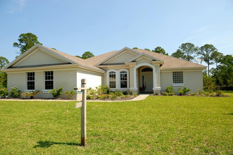 Suburban house with a lush lawn and a for sale sign under a clear blue sky.