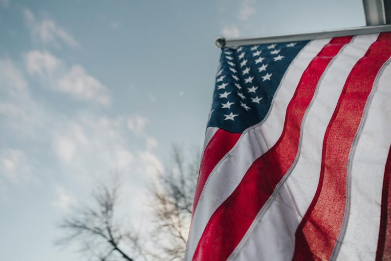Waving American flag against a clear blue sky, symbolizing freedom and patriotism.