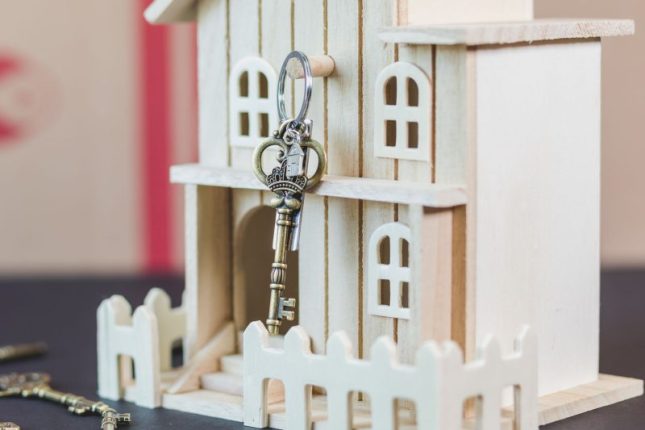 Miniature wooden house next to a vintage key on a wooden surface.