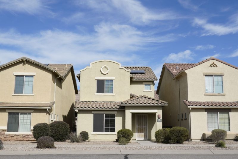 Three adjacent suburban homes in Tucson, Arizona, under a clear blue sky.