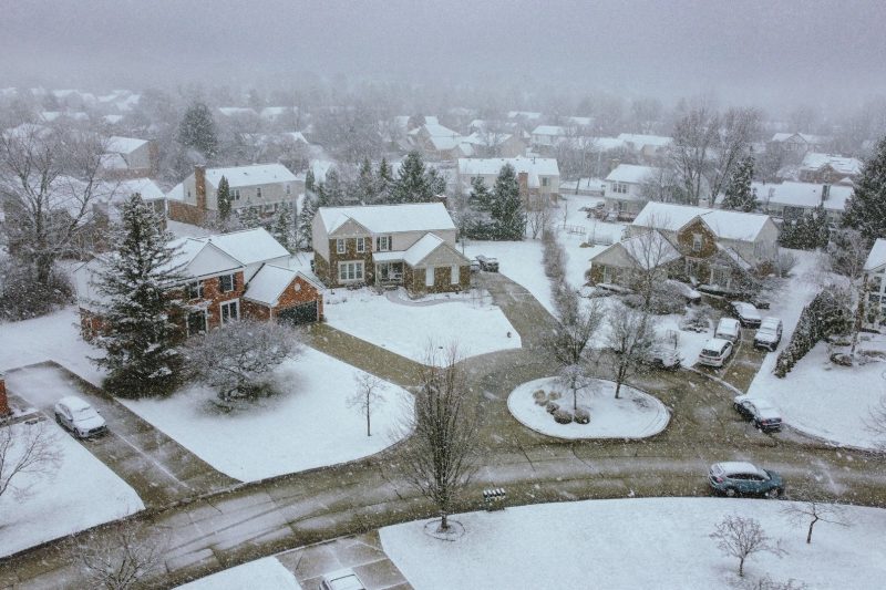 Aerial view of a snow-covered suburban neighborhood with quiet streets and houses nestled among trees.