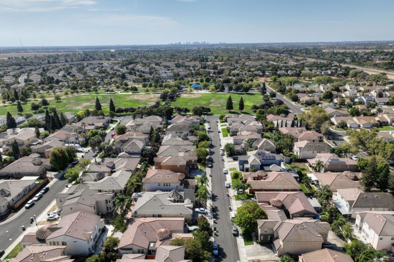 Aerial view of a Sacramento suburb featuring rows of houses surrounded by lush greenery on a sunny day.